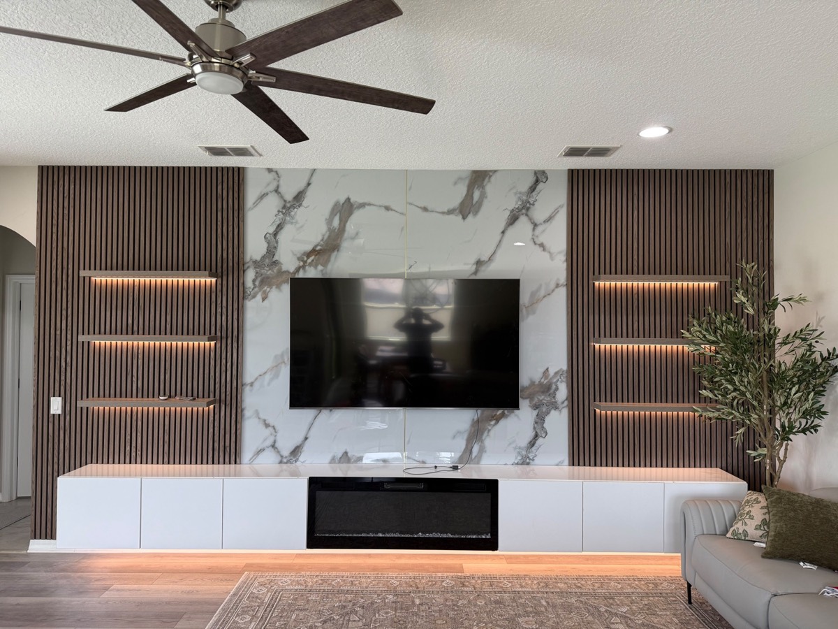 Marble media wall framed by walnut slats with lit floating shelves